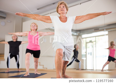 Three mature women perform the exercise by taking the warrior pose II Three mature women perform the exercise by taking the warrior pose II 119577160