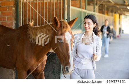 Young woman leads horse out of stable 119577161