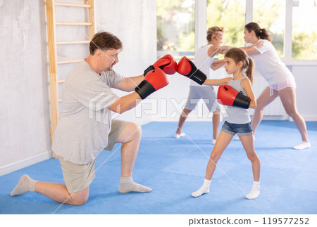 Girl and dad are boxing in gym, father helps child to work out force of blow. Girl and dad are boxing in gym, father helps child to work out force of blow. 119577252
