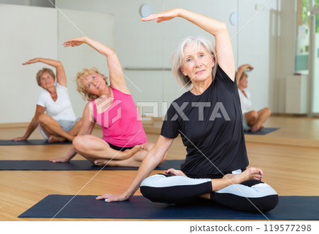 Aged woman doing stretching warm-up during group workout Aged woman doing stretching warm-up during group workout 119577298