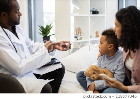 Caring male doctor checks temperature of sick child at home 119577346