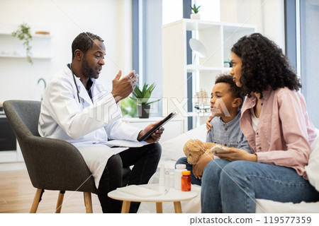 Doctor assists concerned mother with examination of her son 119577359