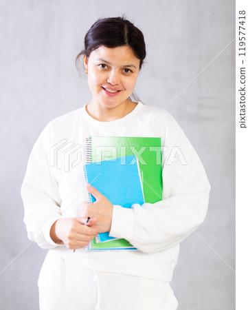 Friendly young female teacher holding workbooks with lecture notes 119577418