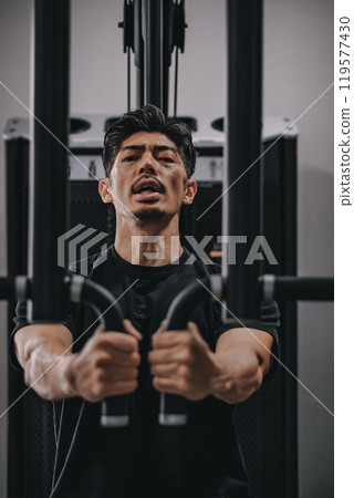 A man in his 40s working out his upper body at the gym 119577430