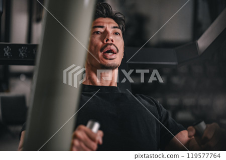 Close-up of a man using machines to train his upper body at the gym Close-up of a man using machines to train his upper body at the gym 119577764