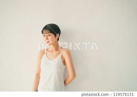 一位身穿白色吊帶背心的年輕女子站在白牆前 一位身穿白色吊帶背心的年輕女子站在白牆前 119578131