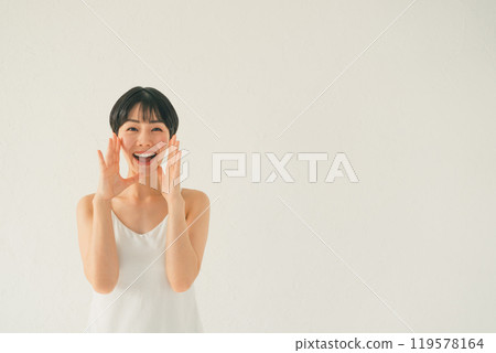 一位穿著吊帶背心的年輕女子用手摀著嘴喊著什麼 一位穿著吊帶背心的年輕女子用手摀著嘴喊著什麼 119578164