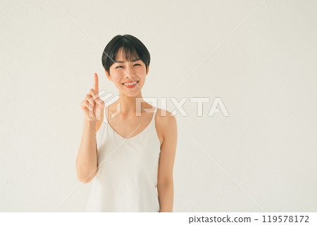 A young woman in a camisole makes a gesture of 1 in front of a white background 119578172