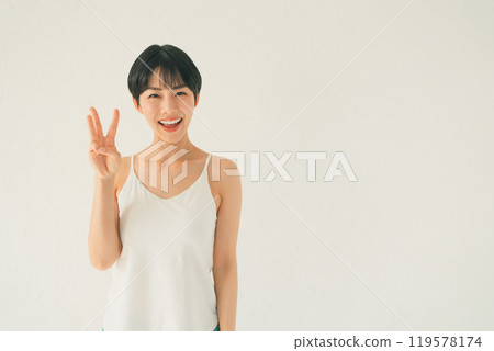 A young woman in a camisole makes a gesture of three in front of a white background 119578174