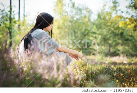 A woman sitting quietly in a peaceful forest clearing surrounded by wildflowers 119578385