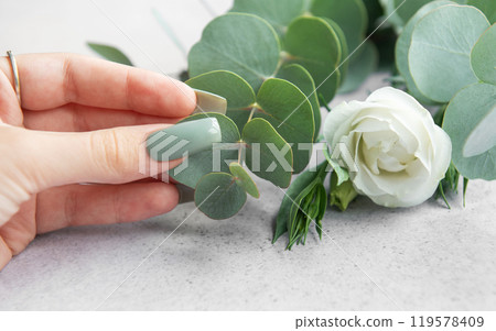 A hand gently touches eucalyptus leaves while preparing a floral arrangement with fresh greenery  119578409