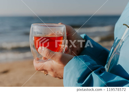 Woman holding a glass of red tea on the beach 119578572