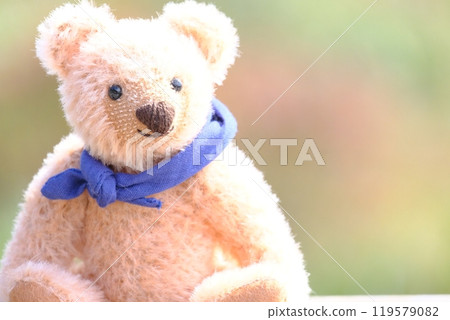 Teddy bear with a scarf, red, blurred autumn leaves in the background, placed on the left, light exposure 119579082