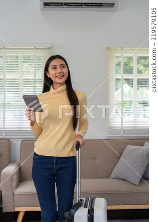 Young Woman Prepares for International Travel with Suitcase and Passport in Modern Living Room Setting Young Woman Prepares for International Travel with Suitcase and Passport in Modern Living Room Setting 119579105