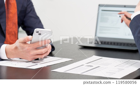 Hands of a businessman using a smartphone at a meeting 119580056