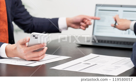 Hands of a businessman using a smartphone at a meeting Hands of a businessman using a smartphone at a meeting 119580057
