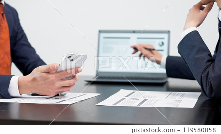 Hands of a businessman using a smartphone at a meeting Hands of a businessman using a smartphone at a meeting 119580058