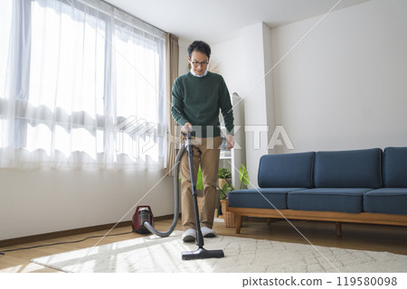 A man in his late 30s vacuuming in his living room A man in his late 30s vacuuming in his living room 119580098