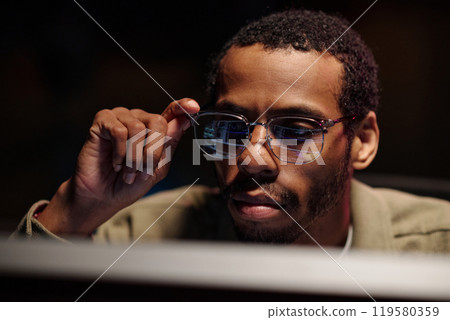 African American Man Adjusting Glasses at Workstation 119580359