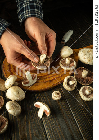 A man sorts Agaricus mushrooms by hand to prepare a delicious breakfast. A set of champignon mushrooms on a dark kitchen table. A delicious recipe from champignon mushrooms 119582363