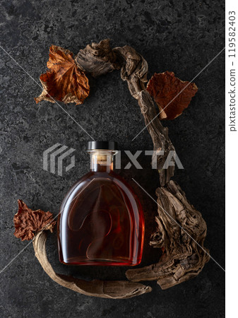 Bottle of brandy and old snags with dried up vine leaves. Bottle of brandy and old snags with dried up vine leaves. 119582403