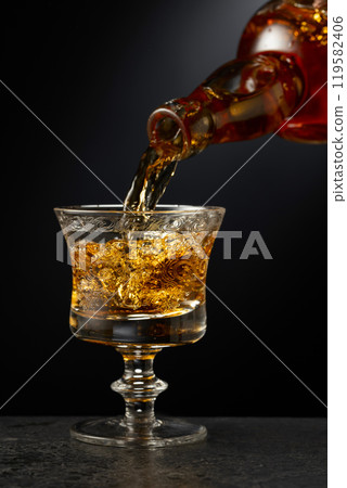 Strong alcoholic drink is poured into a glass. 119582406