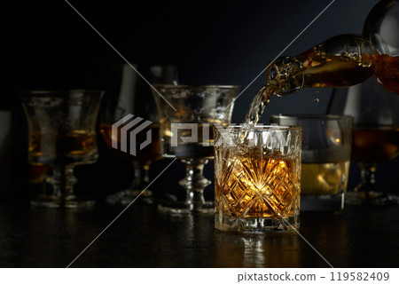 Whiskey is poured from a bottle into a glass. 119582409