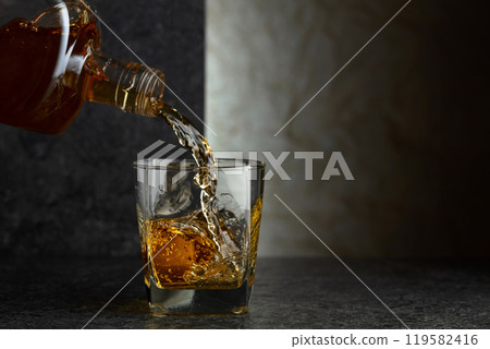 Pouring whiskey from a bottle into a glass. 119582416