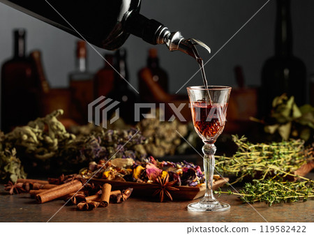 Brown herbal liquor or balm is poured from a vintage bottle into a glass. Brown herbal liquor or balm is poured from a vintage bottle into a glass. 119582422
