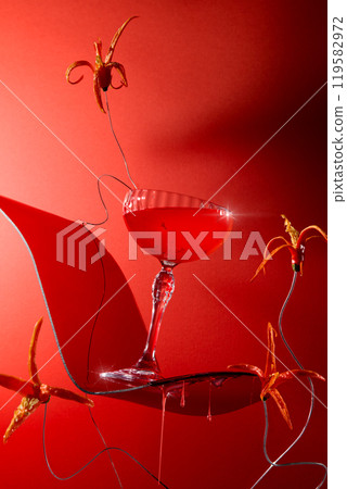 A fiery crimson cocktail tilted to the right on a curvaceous red platform, garnished with cut flowers from hot peppers against a seductive red background. Frontal image template for bar ads. 119582972