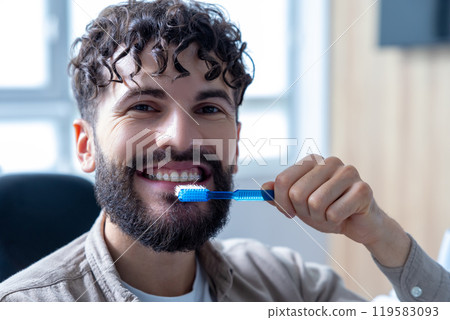 Man with beard in dental clinic holding toothbrush while cleaning teeth maintaining oral hygiene Man with beard in dental clinic holding toothbrush while cleaning teeth maintaining oral hygiene 119583093
