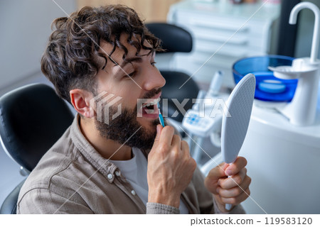 Man with braces meticulously brushing his teeth with interdental brush to maintain oral hygiene 119583120