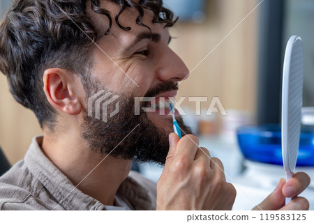Man with crooked teeth and ceramic braces using dental brush to clean around braces 119583125