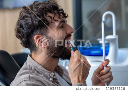 Man with metal braces carefully cleaning his teeth using interdental brush 119583126