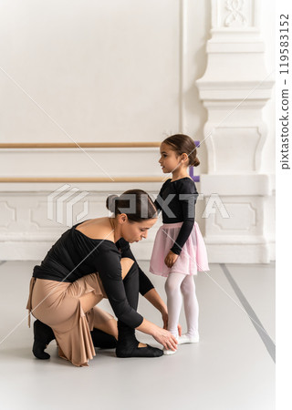 Graceful woman teaching little ballerina in ballet studio 119583152