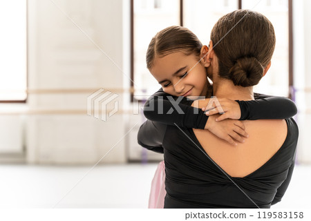 Ballet teacher hugging her young student in studio after creative dance lesson 119583158