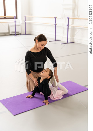 Cute little ballerina practicing ballet with her teacher in studio doing stretching 119583165