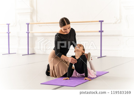 Cute little ballerina practicing ballet with her teacher in studio doing stretching Cute little ballerina practicing ballet with her teacher in studio doing stretching 119583169
