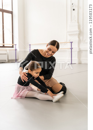 Woman coaching little girl in ballet class guiding her stretching and warming up in studio 119583173