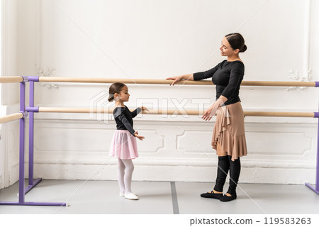 Ballet teacher training little girl at ballet barre in studio 119583263