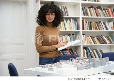 Brunette curly-haired girl working on a project in the library 119583878