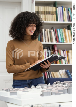 Brunette curly-haired girl working on a project in the library 119583880