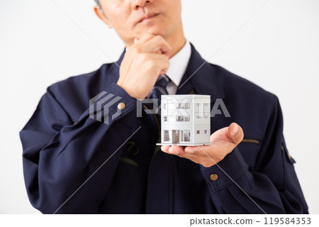 A middle-aged male businessman in work clothes worried about a model of an office building 119584353