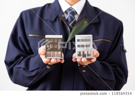 A middle-aged male businessman in work clothes holding a model of an office building 119584354