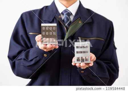 A middle-aged male businessman in work clothes holding a model of an office building A middle-aged male businessman in work clothes holding a model of an office building 119584448