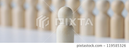 White wooden figure stands against blurred figurines in row White wooden figure stands against blurred figurines in row 119585326