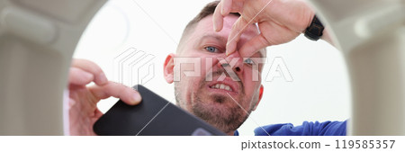 Man takes phone out of toilet bowl pinching nose in disgust 119585357
