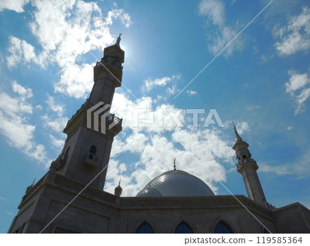 silhouette of mosque against bright blue sky with white clouds, shaded image of islamic religious building, minaret top and dome of muslim church 119585364