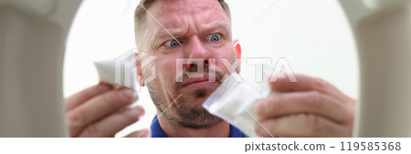 Unshaven man stands over toilet bowl holding narcotics bags 119585368