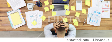 Overworked office worker sits at desk with hands on head 119585393